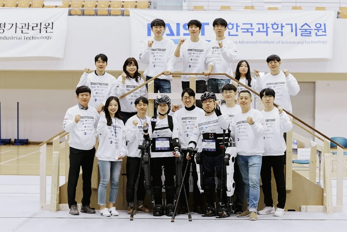 Team photo with the exoskeleton in front of a KAIST banner